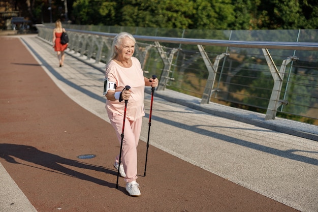 Mulher madura feliz com telefone celular praticando caminhada nórdica na ponte