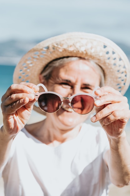 Mulher madura feliz de 50 anos na praia com óculos de sol da moda e um chapéu