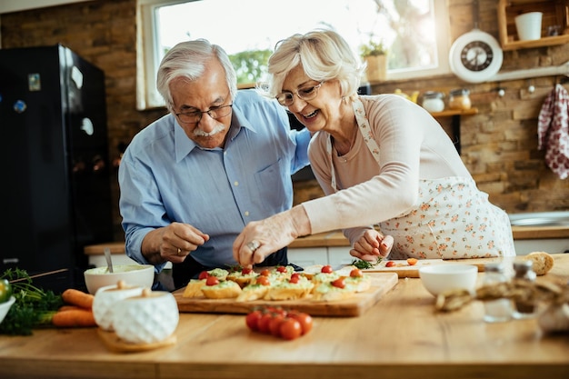 Mulher madura feliz desfrutando com o marido enquanto prepara bruschetta na cozinha