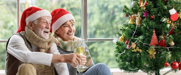 Mulher madura feliz e homem idoso examinando o presente enquanto está sentado no tapete entre árvores de Natal decoradas contra a janela de casa