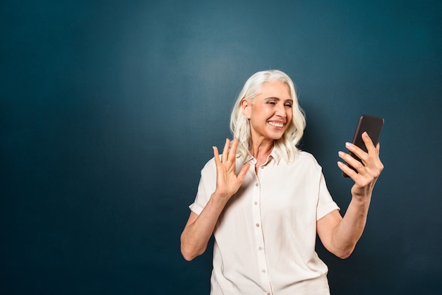 Mulher madura feliz falando com os amigos pelo telefone móvel acenando.