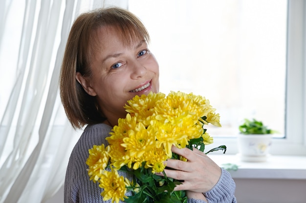 Mulher madura feliz segurando uma braçada de flores amarelas