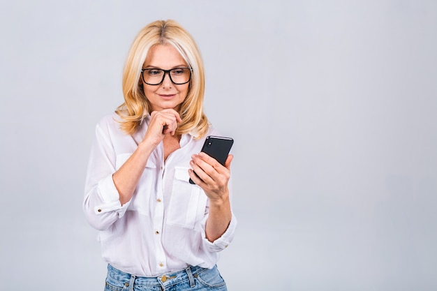 Mulher madura feliz sênior segurando smartphone usando aplicativos móveis online, sorrindo, velha senhora de meia-idade, mensagens de texto sms, conversando no telefone, olhando para o celular isolado no fundo cinza branco