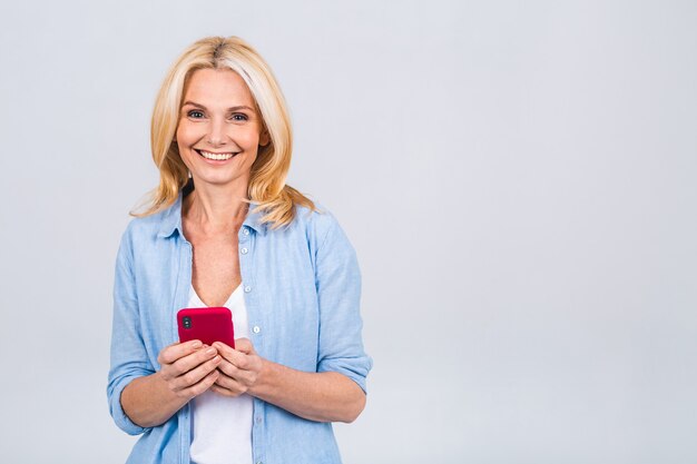 Mulher madura feliz sênior segurando smartphone usando aplicativos móveis online, sorrindo, velha senhora de meia-idade, mensagens de texto sms, conversando no telefone, olhando para o celular isolado no fundo cinza branco