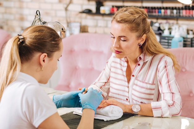 Mulher madura focada olhando para as unhas enquanto a manicure cuida das unhas