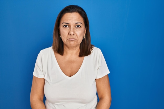 Mulher madura hispânica em pé sobre fundo azul deprimido e preocupado com angústia, chorando com raiva e medo. expressão triste.