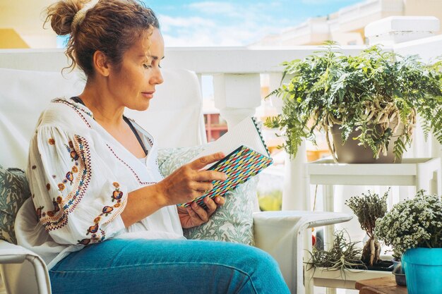 Foto mulher madura lendo um livro sentada na varanda