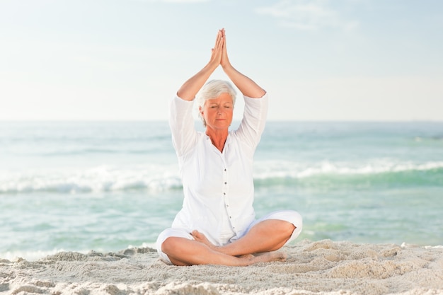 Mulher madura praticando yoga na praia