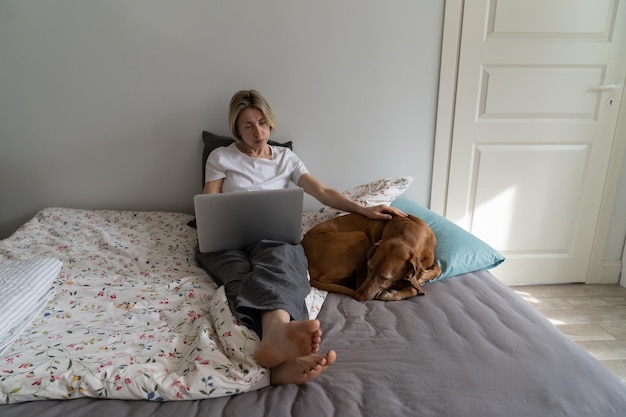 Mulher madura rola a Internet procurando vaga de emprego on-line via laptop na cama por cachorro