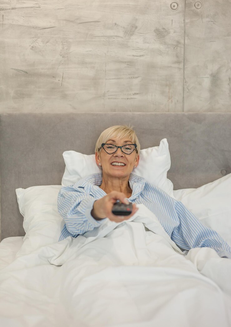Foto mulher madura sorridente a ver televisão na cama.