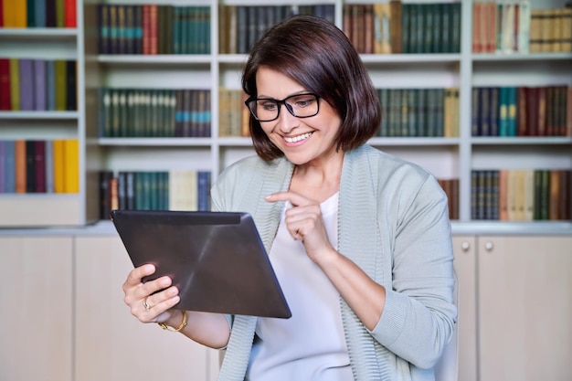 Mulher madura sorridente de negócios usando tablet digital no escritório da biblioteca