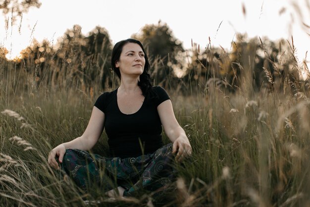 Foto mulher madura sorridente sentada no campo durante o pôr do sol