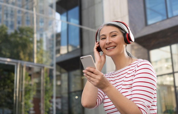 Mulher madura sorridente usando fone de ouvido sem fio ouvindo música na rua