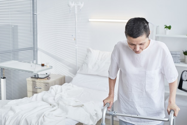 Mulher madura tentando andar com o andador na enfermaria do hospital