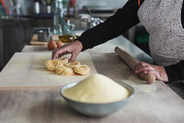 Mulher madura trabalhando dentro da fábrica de massas fazendo tagliatelle fresco