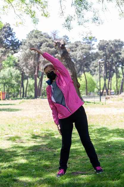 Mulher madura treina em um parque fazendo alongamentos enquanto ouve música ou algum podcast