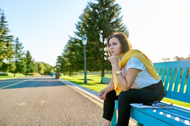 Mulher madura triste cansada sentada no banco no parque cópia espaço Depressão dor de cabeça menopausa problemas de meia-idade conceito de idade de saúde