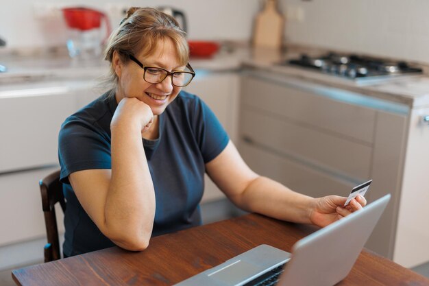 Mulher madura usando cartão de crédito fazendo pagamento online em casa