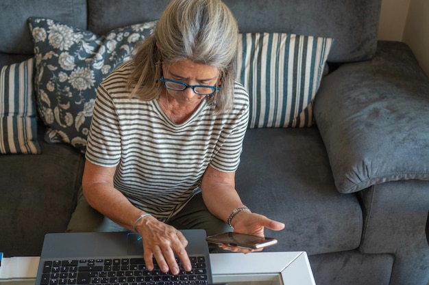 Mulher madura usando telefone celular e laptop em casa