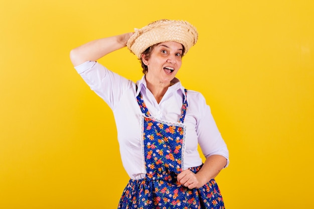 Mulher madura, vestida com roupas típicas da Festa Junina, segurando o chapéu de palha