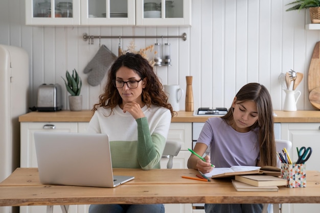 Mulher mãe freelancer trabalhando remotamente no laptop com criança sentada ao lado e fazendo lição de casa