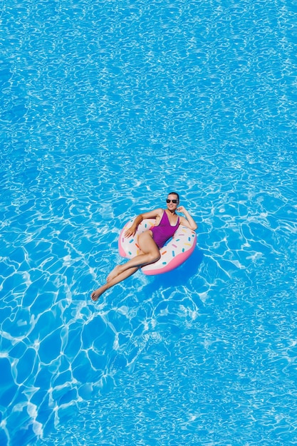 Mulher magra em óculos de sol na piscina em um anel de natação inflável em um maiô brilhante foto de verão fotografia de natação fotos de mulher de verão moda praia