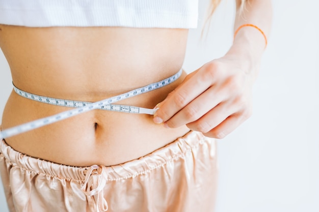 Mulher magra medindo o tamanho da cintura com fita métrica em fundo branco. perda de peso com sucesso.
