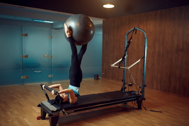 Mulher magro em roupas esportivas, pilates treinando com bola na máquina de exercícios no ginásio. Exercício de aptidão no clube desportivo.