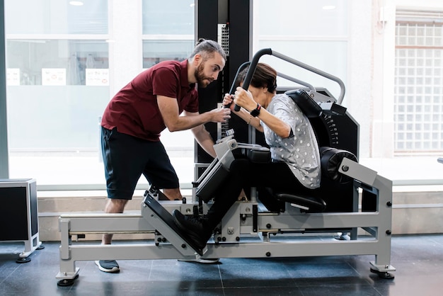 Mulher mais velha malhando nas máquinas na academia com seu personal trainer