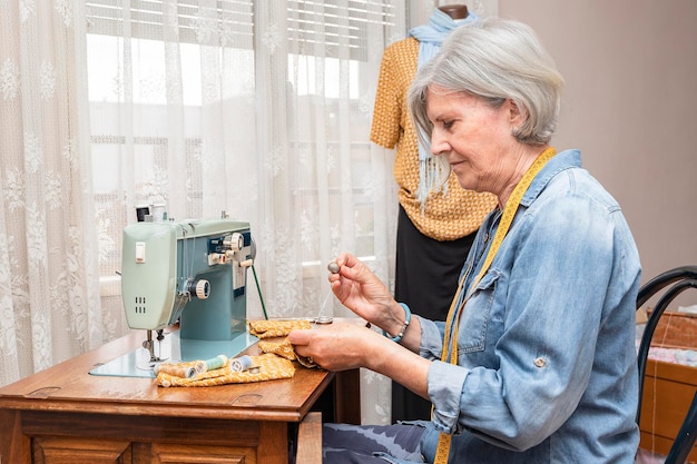 Mulher mais velha na frente de uma máquina de costura costurando à mão um pedaço de tecido laranja