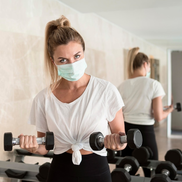 Foto mulher malhando com pesos na academia enquanto usa máscara médica