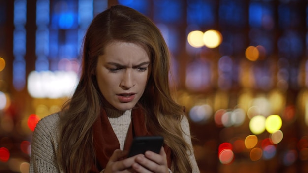 Mulher malvada lendo sms telefone celular ao ar livre Garota irritada olhando a tela do telefone