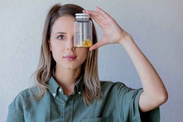 Mulher mantém o frasco transparente com comprimidos ao nível dos olhos. vista lateral