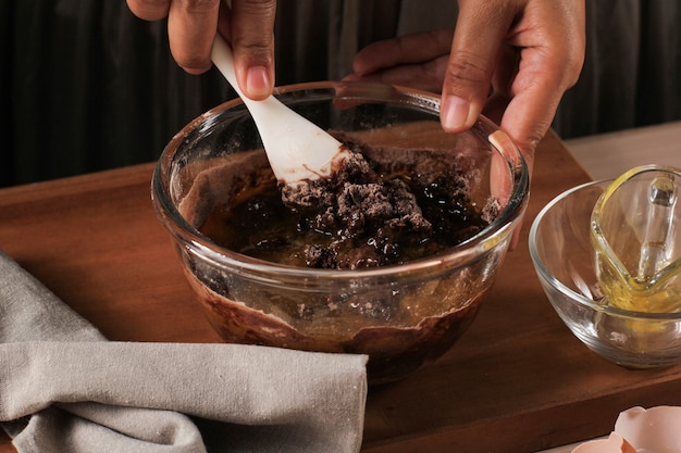 Foto mulher mão misturada massa de chocolate em uma tigela transparente com espátula branca, preparação passo a passo para assar na cozinha, fazer bolo de chocolate ou brownies