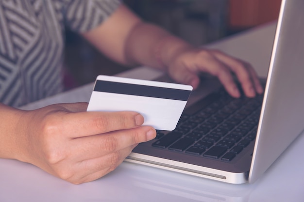 Mulher mão segurando o cartão de crédito e usando o laptop fazendo o pagamento on-line, compras on-line