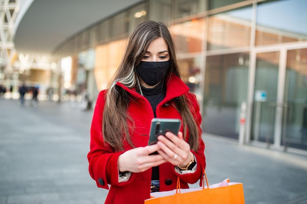 Mulher mascarada andando em uma cidade enquanto estiver usando seu telefone celular