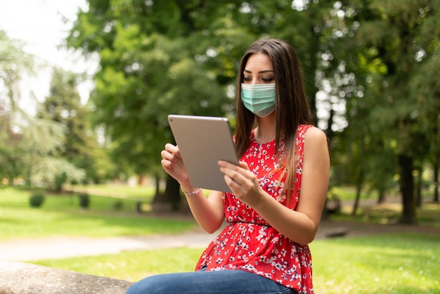 Mulher mascarada usando um tablet no parque