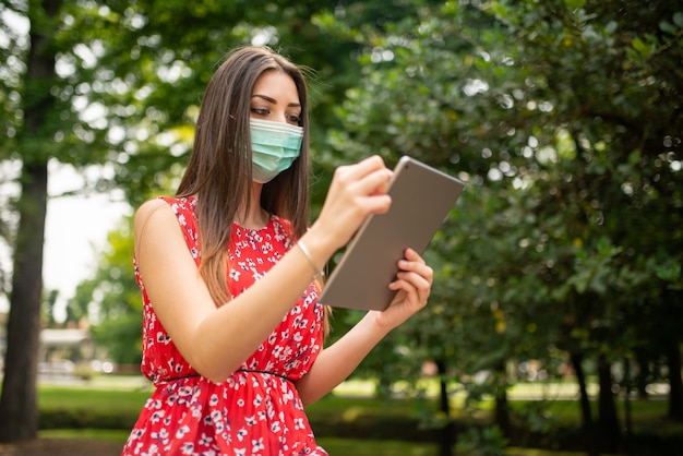 Mulher mascarada usando um tablet no parque