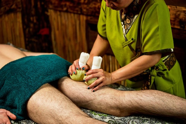 Mulher massageia a perna do paciente com sacos de ervas no salão spa