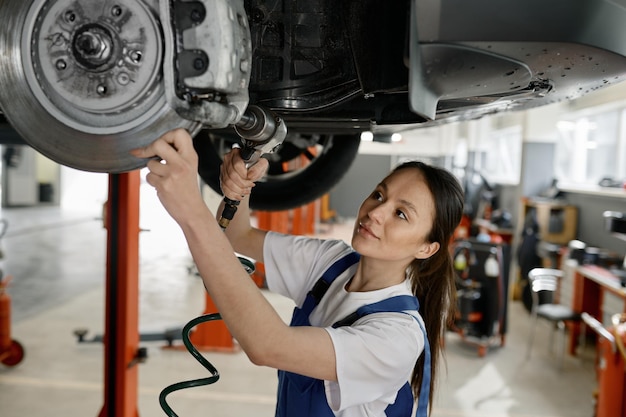 Mulher mecânica automática a corrigir um problema com o equipamento de marcha do automóvel numa estação de serviço.