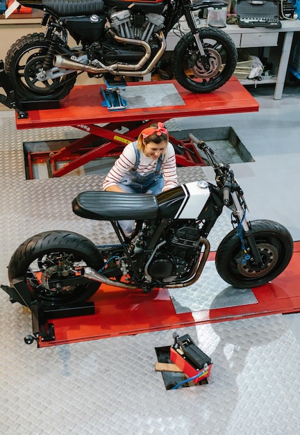 Foto mulher mecânica revisando motocicleta personalizada na fábrica