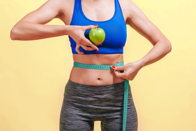 Foto mulher mede a cintura e mostra maçã verde na parede amarela
