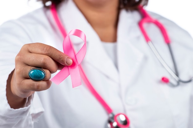 Mulher médica com estetoscópio rosa segurando uma fita rosa de câncer de mama em um fundo branco.