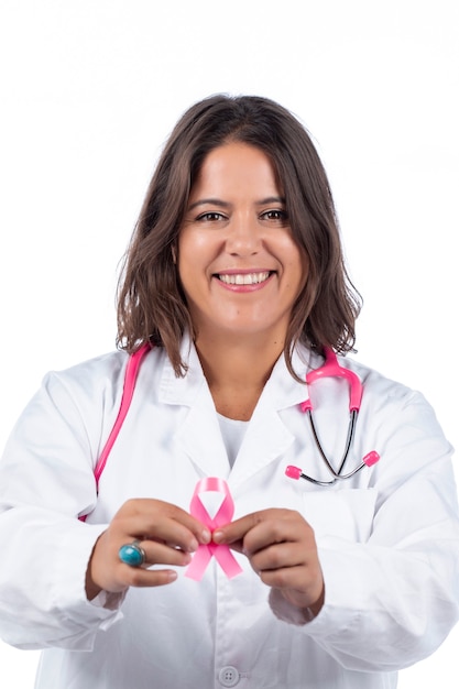 Mulher médica com estetoscópio rosa segurando uma fita rosa de câncer de mama em um fundo branco.