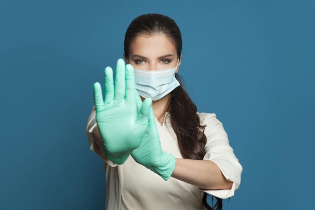 Mulher médica com máscara médica protetora mostrando um gesto de parada em fundo azul Conceito de vacinação de segurança médica e proteção contra o vírus covid-19
