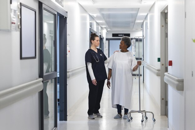 Mulher médica conversando com paciente idosa com gotejamento no corredor do hospital