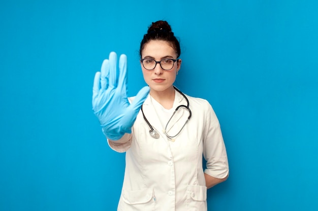 Mulher médica de uniforme mostra gesto de parada com a mão sobre fundo azul