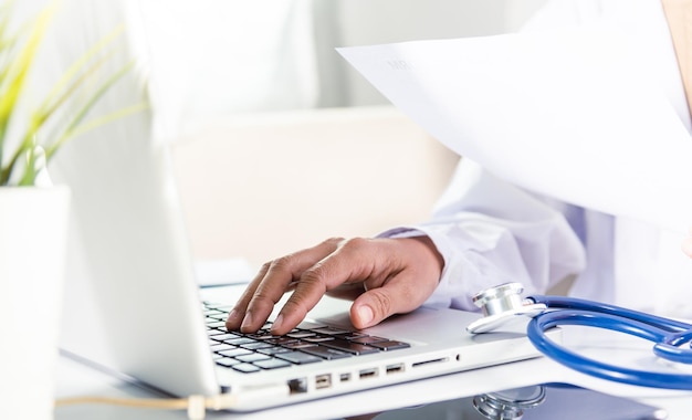 Mulher médica digitando informações da prescrição do paciente do formulário de histórico médico da papelada no laptop