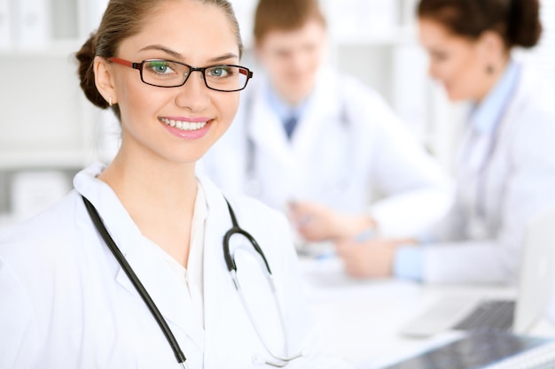 Mulher médica feliz com equipe médica no hospital sentado à mesa Óculos de armação vermelha