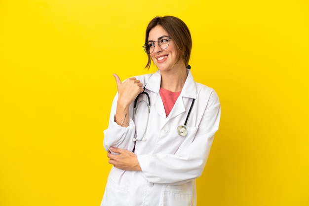 Mulher médica isolada em fundo amarelo apontando para o lado para apresentar um produto